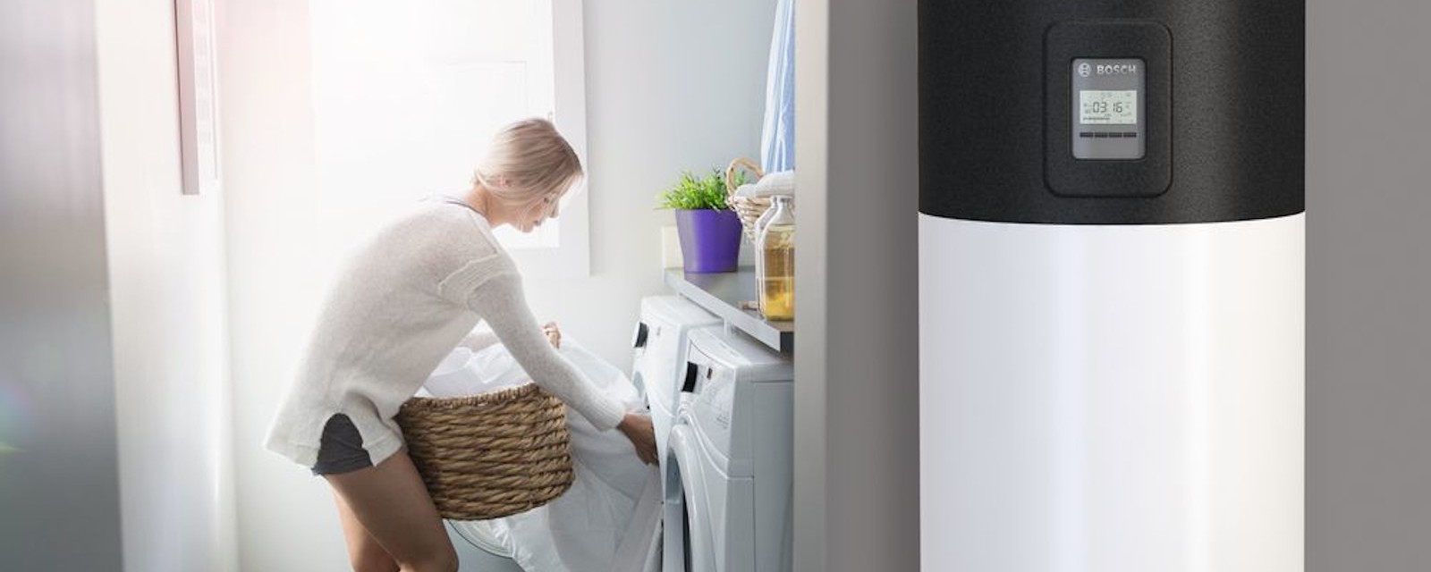 Eine Frau räumt Wäsche in die Waschmaschine, im Vordergrund ist eine Wärmepumpe zu sehen.